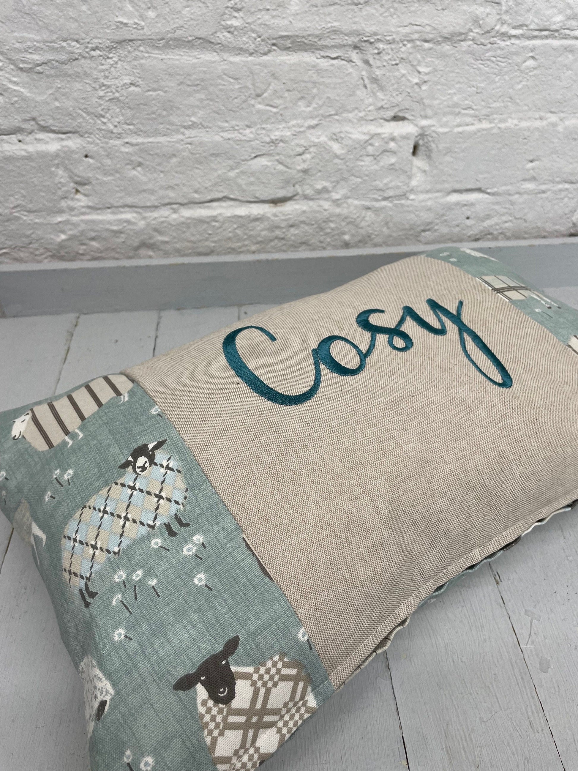 Cosy sheep in jumpers rectangle cushion with the word Cosy embroidered in duckegg on a coordinating taupe panel. Duck egg sheep in jumpers