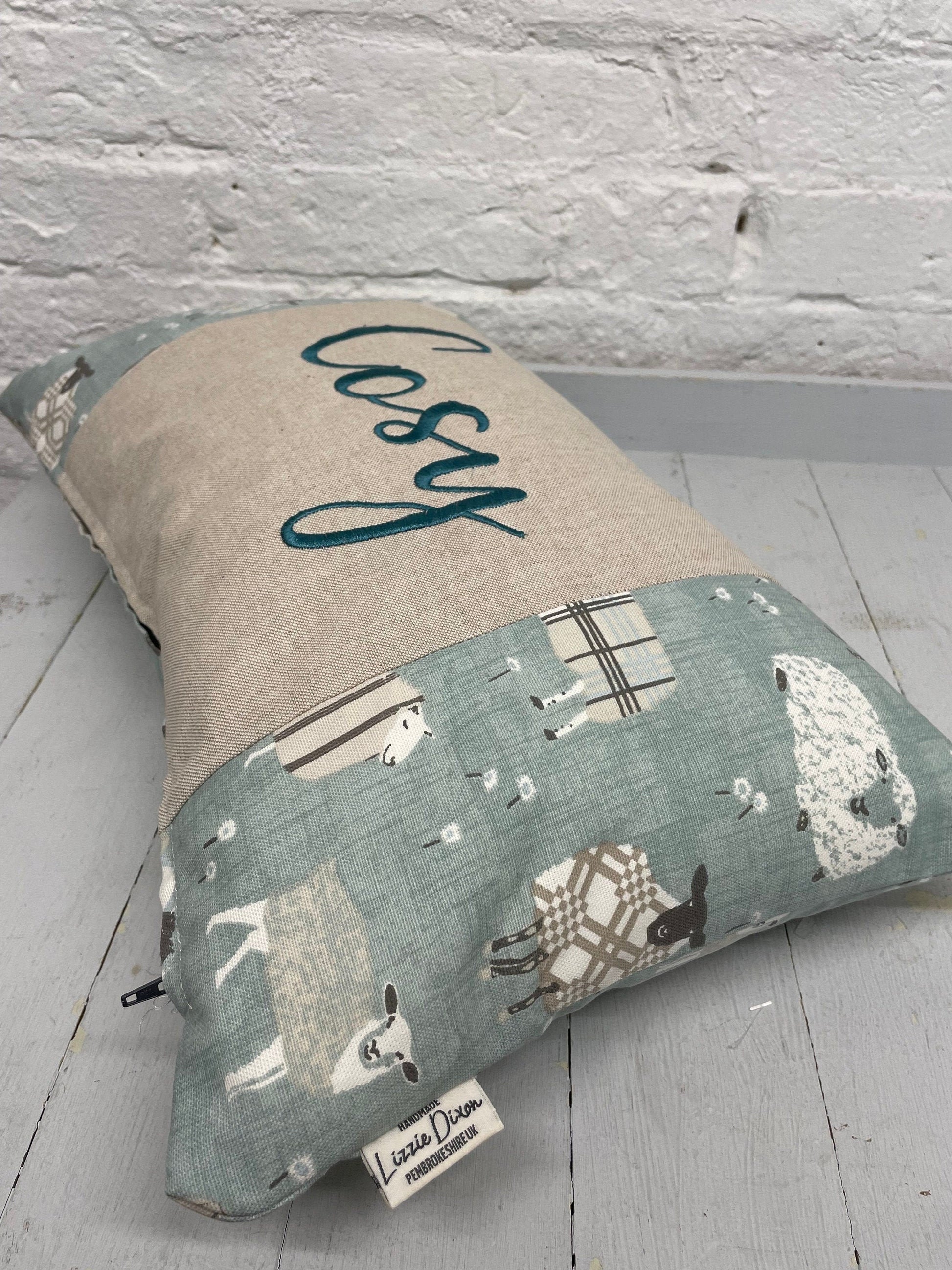 Cosy sheep in jumpers rectangle cushion with the word Cosy embroidered in duckegg on a coordinating taupe panel. Duck egg sheep in jumpers