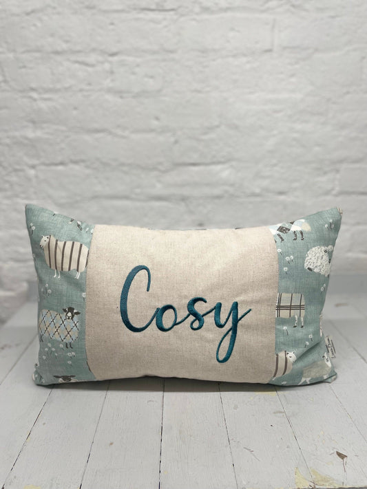 Cosy sheep in jumpers rectangle cushion with the word Cosy embroidered in duckegg on a coordinating taupe panel. Duck egg sheep in jumpers