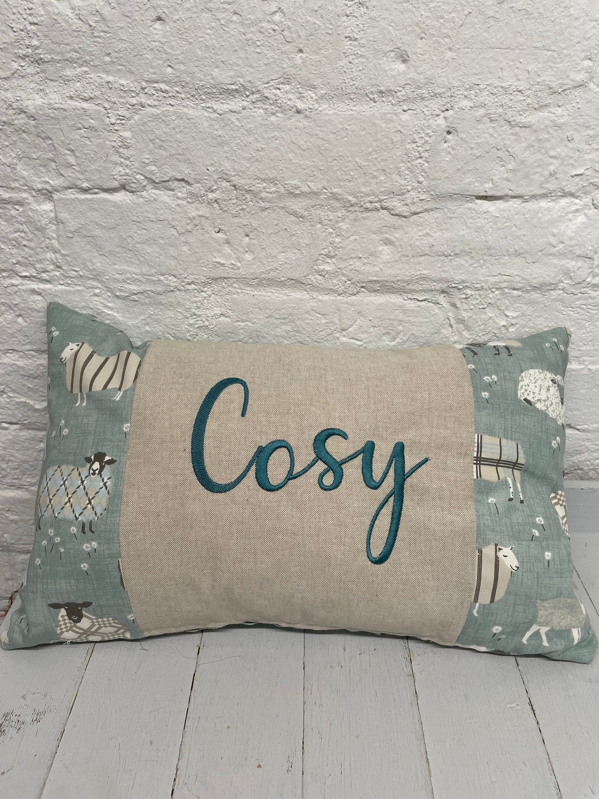 Cosy sheep in jumpers rectangle cushion with the word Cosy embroidered in duckegg on a coordinating taupe panel. Duck egg sheep in jumpers