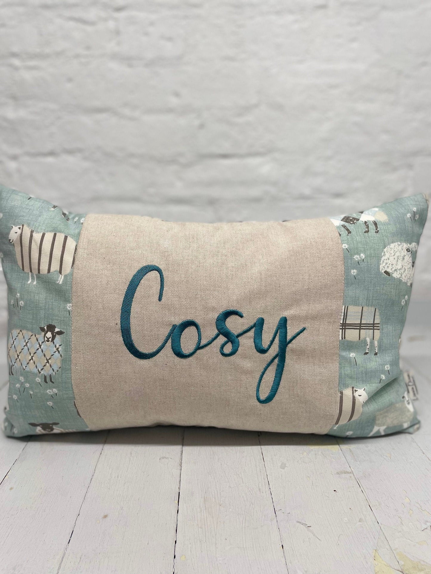 Cosy sheep in jumpers rectangle cushion with the word Cosy embroidered in duckegg on a coordinating taupe panel. Duck egg sheep in jumpers